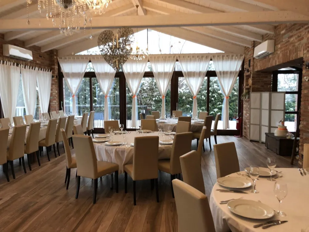 La sala con travi a vista e grandi vetrate sul verde, tavoli rotondi apparecchiati